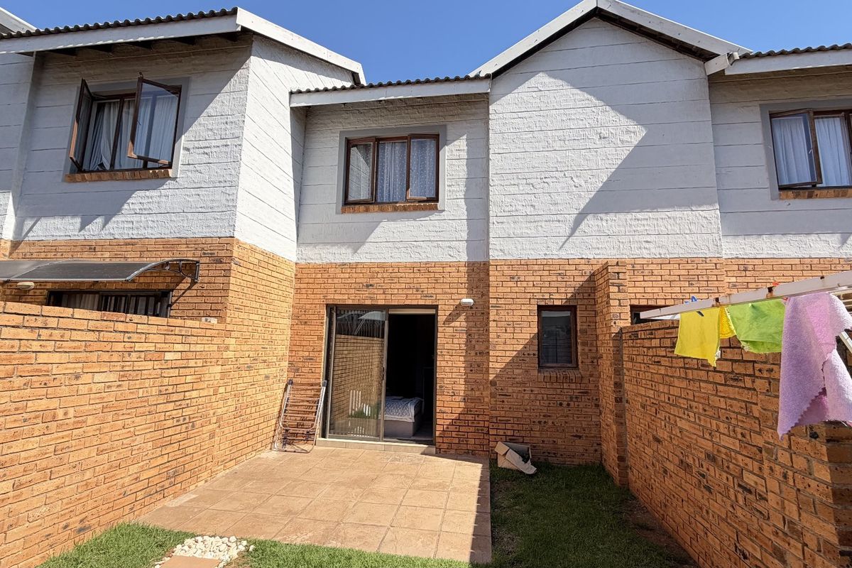 Rear view of a townhouse featuring a private brick-walled courtyard, tiled patio area, and sliding door access to the interior.