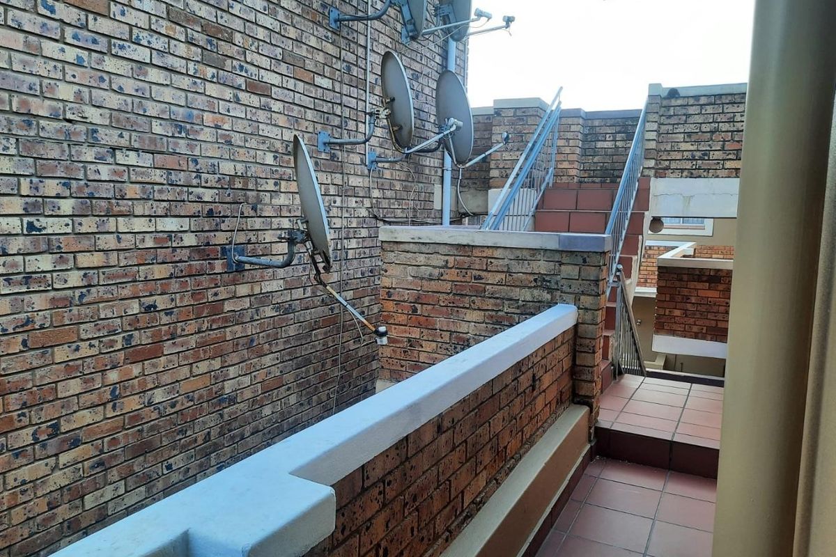 Exterior view of an apartment building featuring a brick facade, tiled staircase, and metal handrails with multiple satellite dishes mounted to the wall.