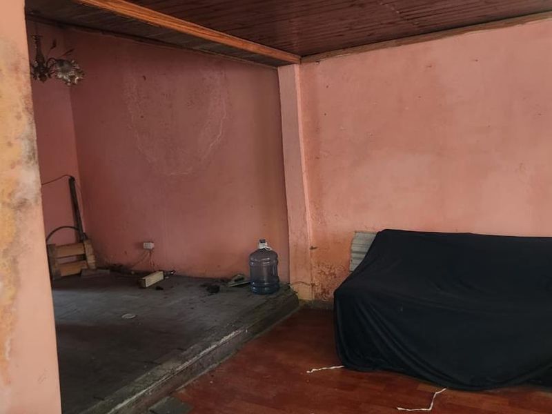 A living area featuring a timber ceiling and a raised floor platform, currently requiring significant cosmetic renovation and wall repairs.