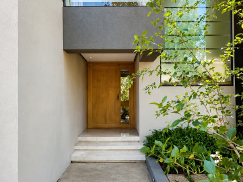 Modern front entrance featuring a natural timber door, stone steps, and a clean concrete pathway with integrated landscaping and recessed lighting.