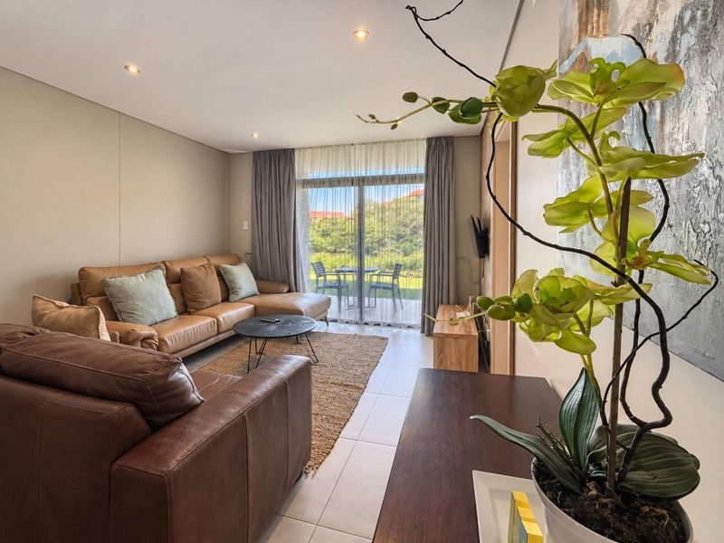 A bright and modern living room featuring tiled flooring, recessed downlights, and a large sliding glass door providing access to an outdoor patio area.