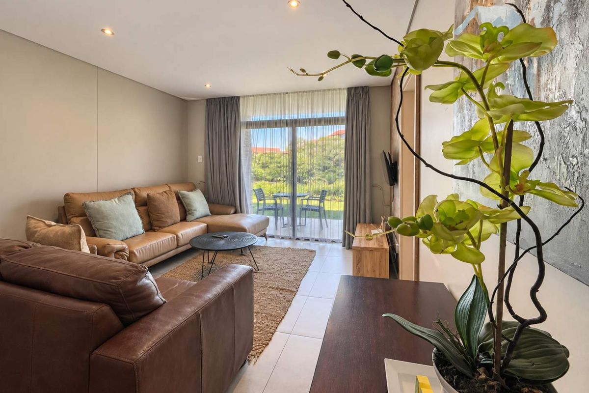 A bright and modern living room featuring tiled flooring, recessed downlights, and a large sliding glass door providing access to an outdoor patio area.