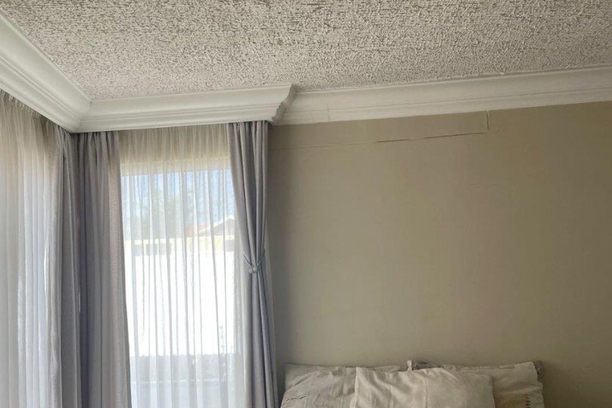 A bedroom featuring tiled flooring, crown molding, and a textured popcorn ceiling, with visible wall cracking requiring maintenance.