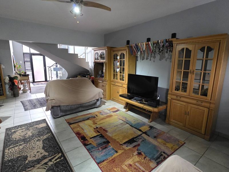 Spacious living area featuring tiled flooring, a central staircase, and a ceiling fan, offering a functional layout with potential for modern updates.