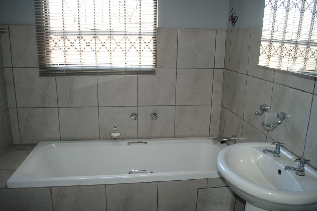 A functional bathroom featuring a standard bathtub, pedestal basin, and tiled walls with window blinds.
