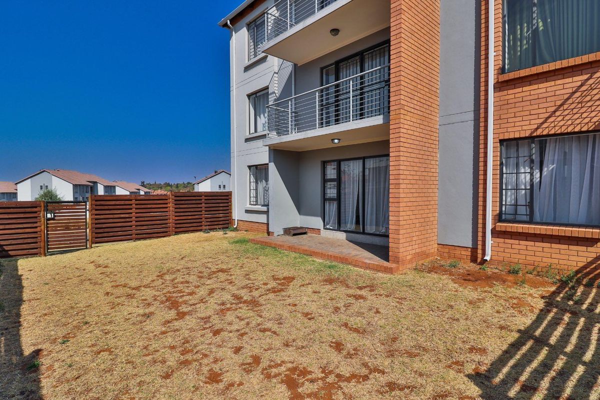 Rear view of the apartment building featuring a private garden, paved patio area, and balconies with metal railings.