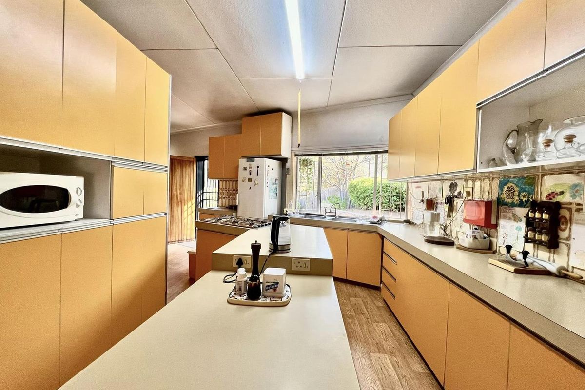 A dated kitchen featuring extensive yellow cabinetry, laminate countertops, a central island, and a functional layout with a window overlooking the garden.