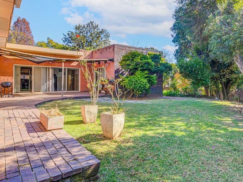 A rear view of the property featuring a brick paved patio, covered outdoor area, and a spacious landscaped garden with mature trees.