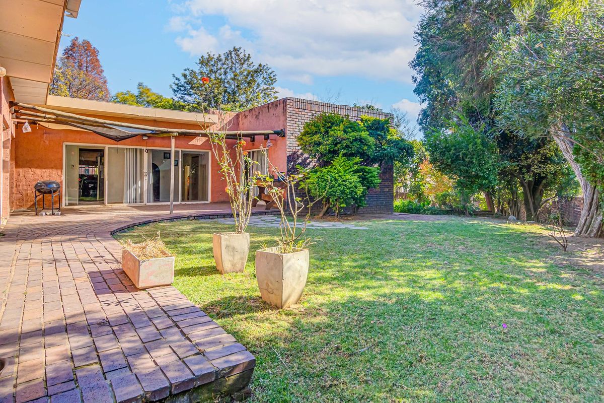 A rear view of the property featuring a brick paved patio, covered outdoor area, and a spacious landscaped garden with mature trees.