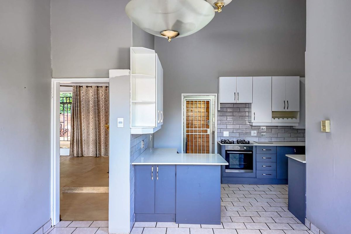 A functional kitchen featuring blue lower cabinetry, white upper cabinets, a built-in oven with gas hob, and tiled flooring with a breakfast counter.