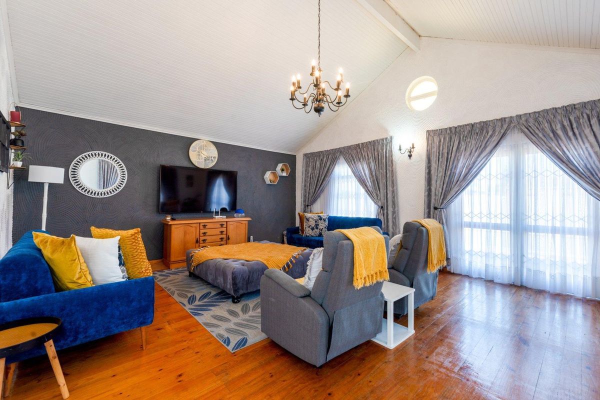 Spacious living room featuring high vaulted ceilings, warm timber flooring, a striking dark feature wall, and abundant natural light through large windows.