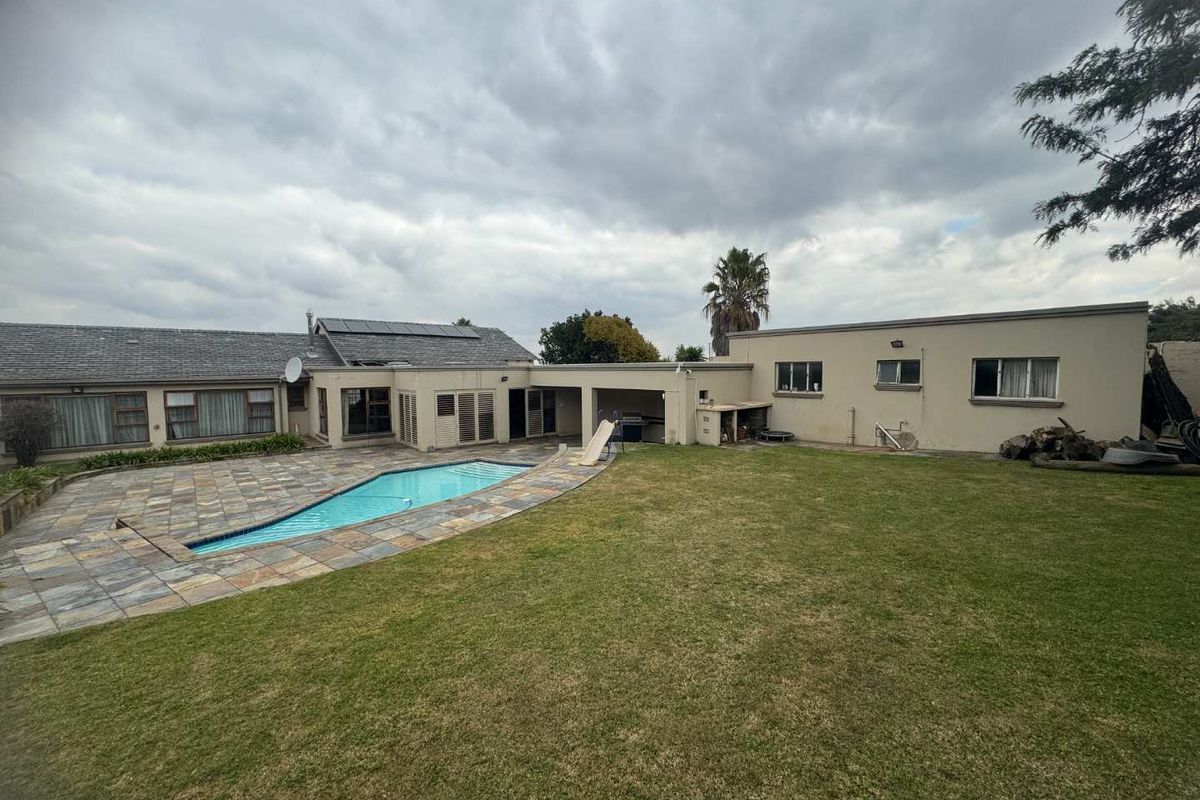 Spacious rear garden featuring a swimming pool with stone paving, a covered patio area, and a large lawn, ideal for outdoor entertaining.