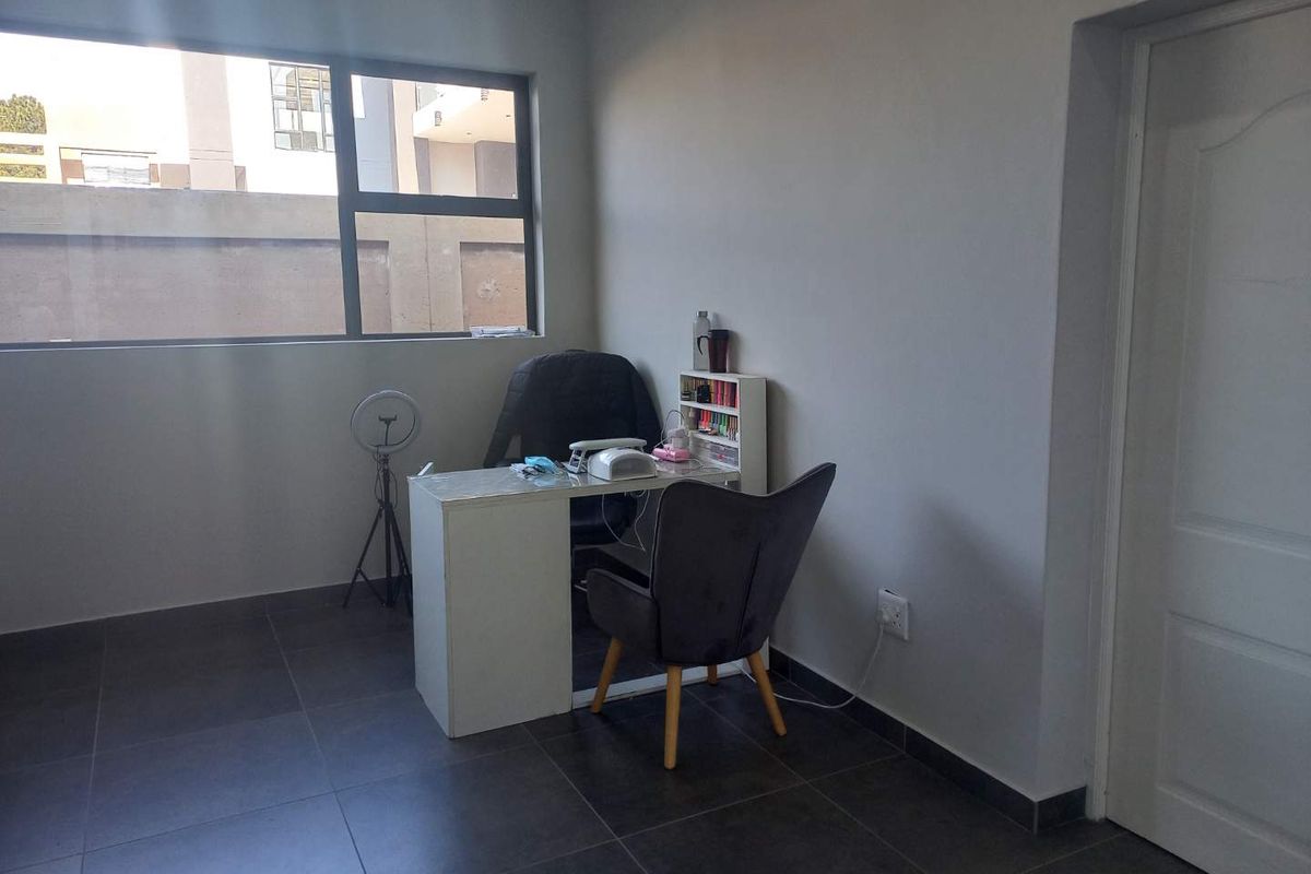 A functional room featuring dark tiled flooring and large aluminium-framed windows, currently utilized as a workspace.