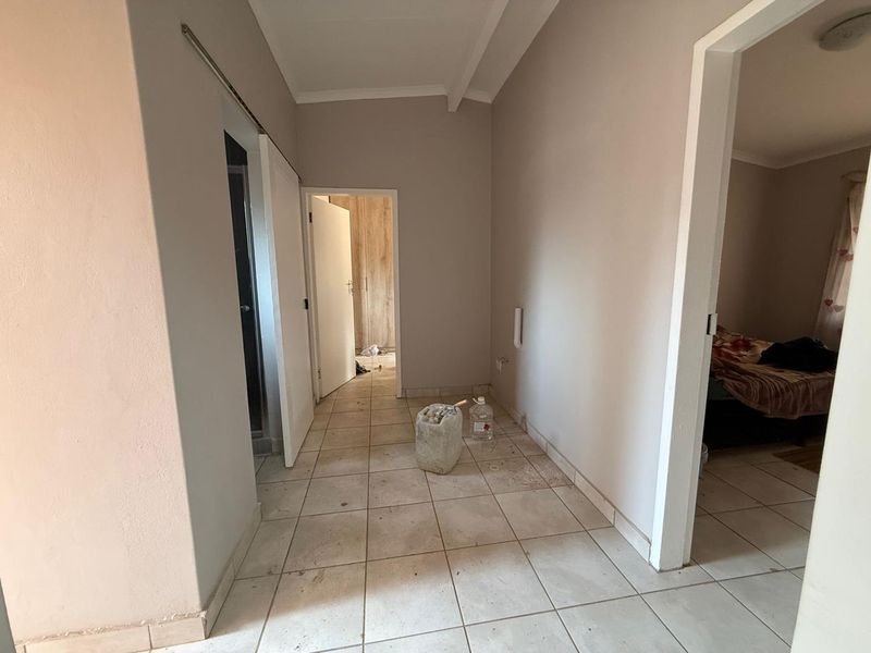 A functional hallway area featuring tiled flooring and access to adjacent rooms, including a bedroom with built-in cupboards.