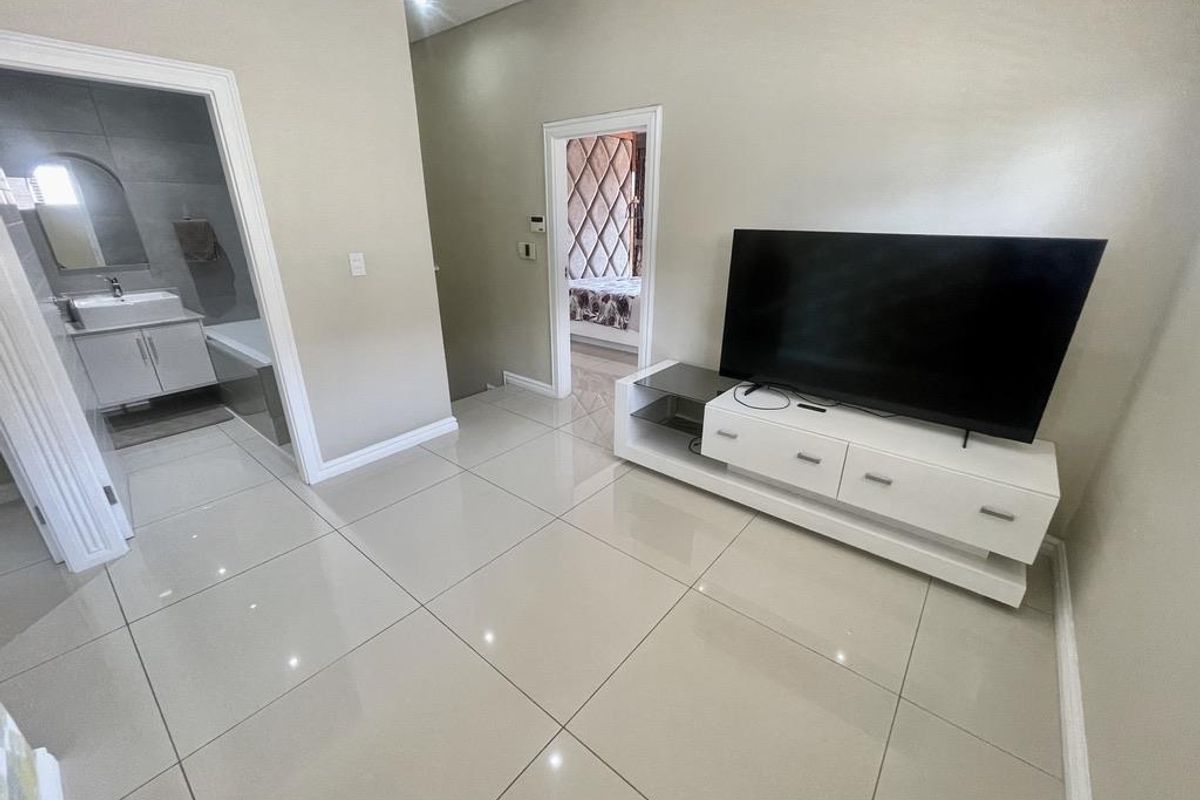 A bright living area featuring large format floor tiles, leading into an en-suite bathroom and a secondary bedroom.