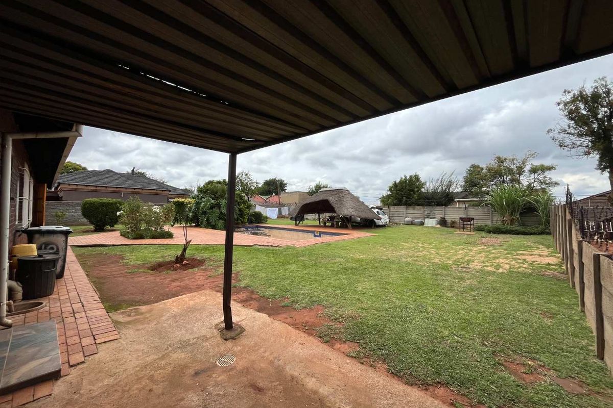 Spacious rear garden featuring a covered patio, swimming pool, and a traditional thatched lapa, enclosed by precast concrete boundary walls.