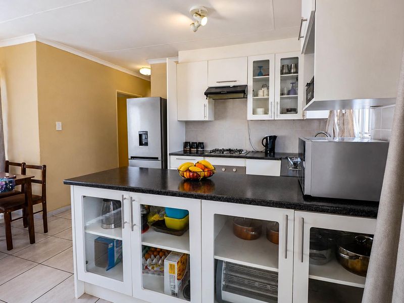 A functional kitchen featuring white cabinetry, a dark countertop island, gas hob, extractor fan, and tiled flooring, providing a practical workspace.