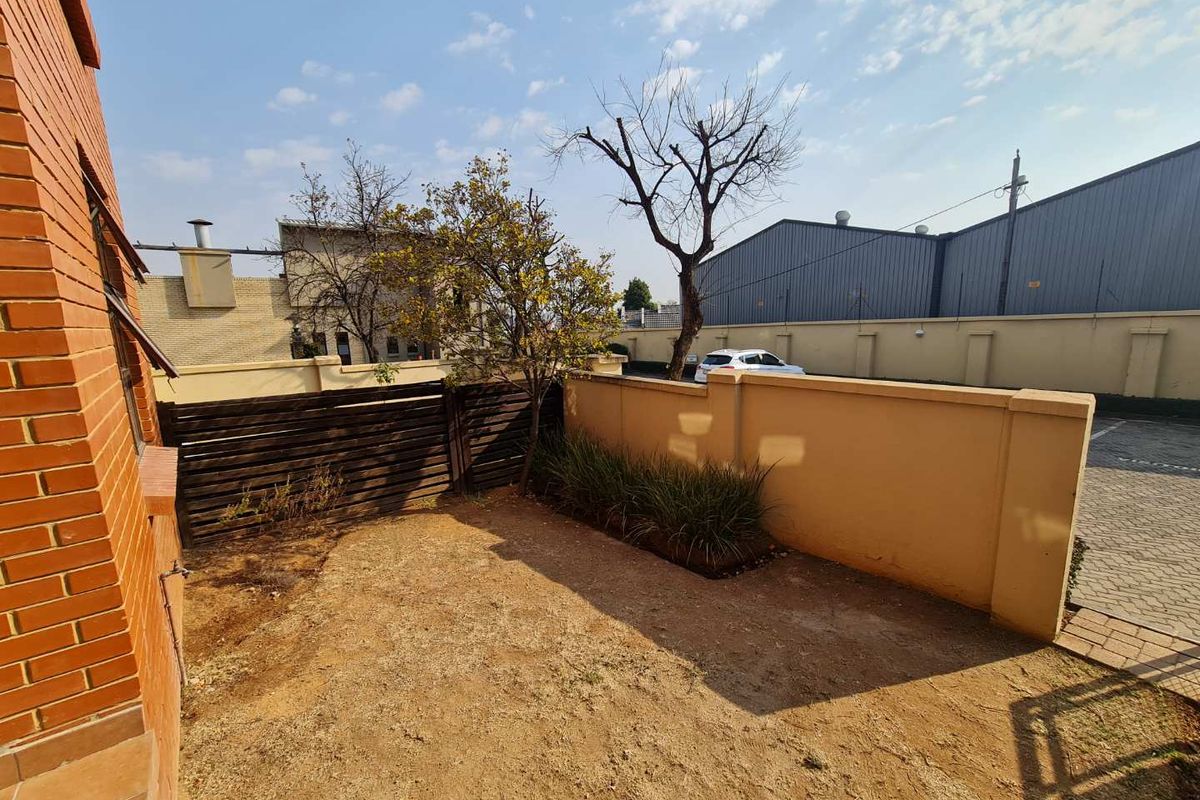 A private rear garden area featuring a brick boundary wall, timber fencing, and a small patch of lawn adjacent to the apartment building.