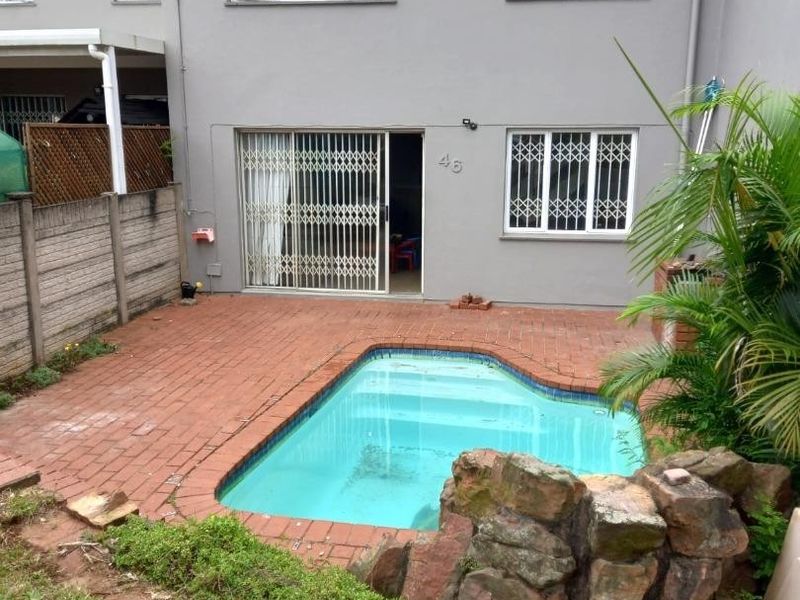 Rear view of the townhouse featuring a private swimming pool, brick-paved patio area, and secure sliding door access to the living space.