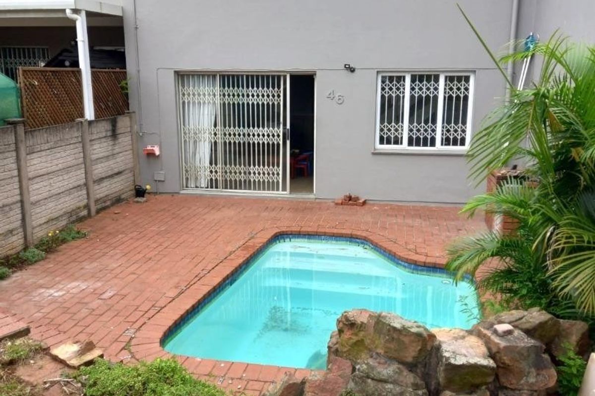 Rear view of the townhouse featuring a private swimming pool, brick-paved patio area, and secure sliding door access to the living space.