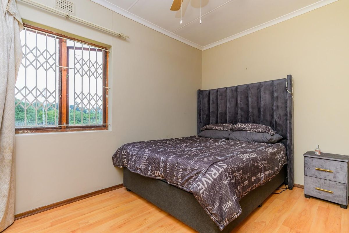 A standard bedroom featuring laminate flooring, a ceiling fan, and a window fitted with a security gate.