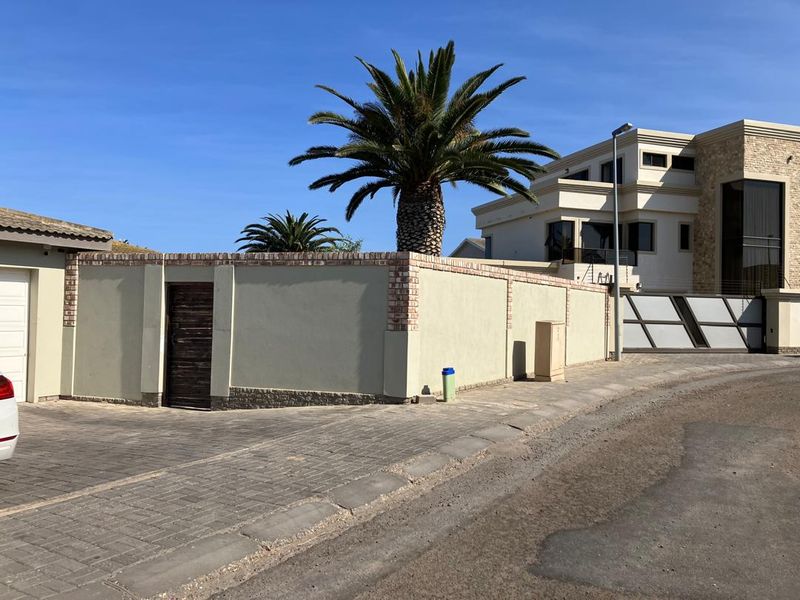 Front exterior view of the property featuring a paved driveway, secure boundary wall with pedestrian gate, and a modern multi-story house facade.