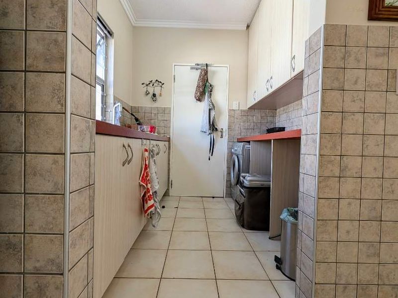 A functional scullery area featuring built-in cabinetry, tiled splashbacks, and dedicated plumbing connections for laundry appliances.
