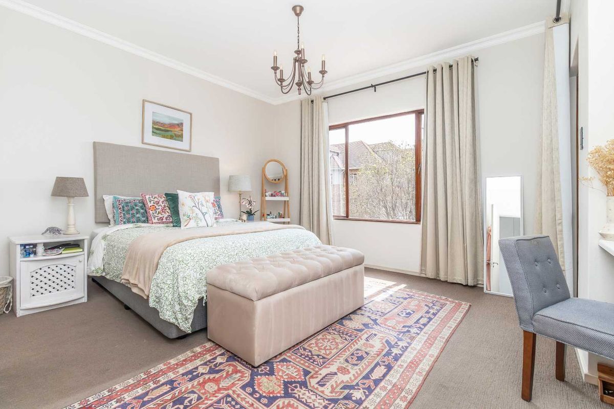 A well-maintained bedroom featuring crown molding, a central chandelier, and a large window allowing for natural light.