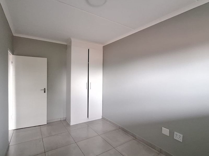 A clean, empty bedroom featuring neutral grey walls, tiled flooring, and a built-in white wardrobe.