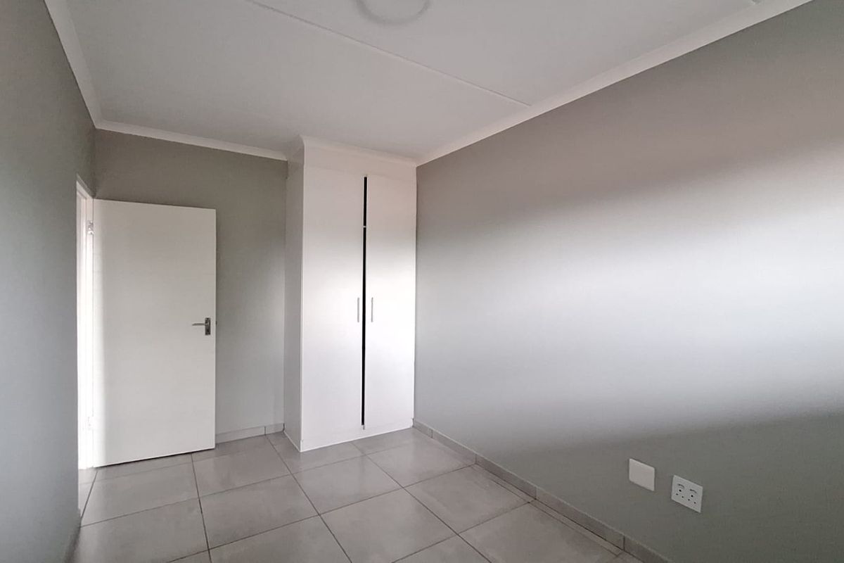 A clean, empty bedroom featuring neutral grey walls, tiled flooring, and a built-in white wardrobe.
