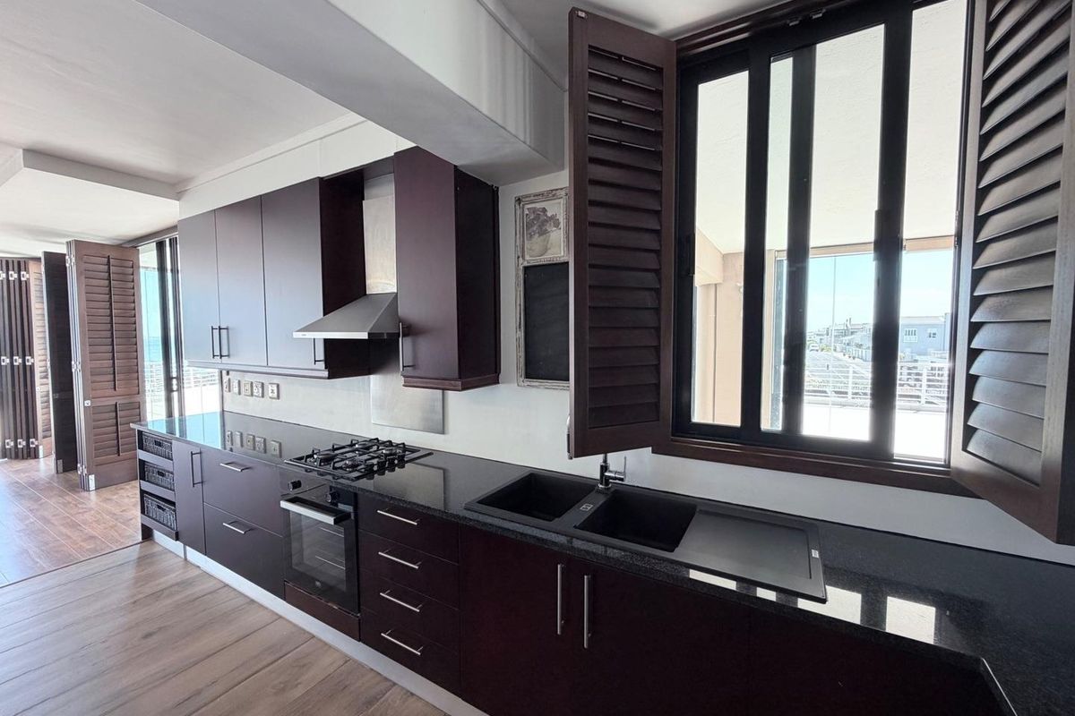 Modern kitchen featuring dark cabinetry, granite countertops, integrated gas hob, oven, extractor fan, and double sink with plantation shutters.