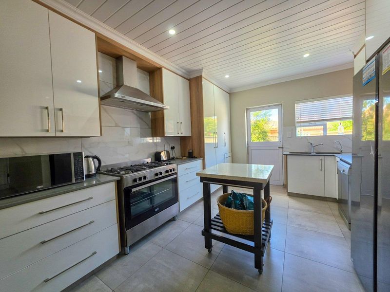 Modern kitchen featuring white cabinetry, stone countertops, gas stove with extractor fan, tiled flooring, and a bright, functional layout with direct outdoor access.