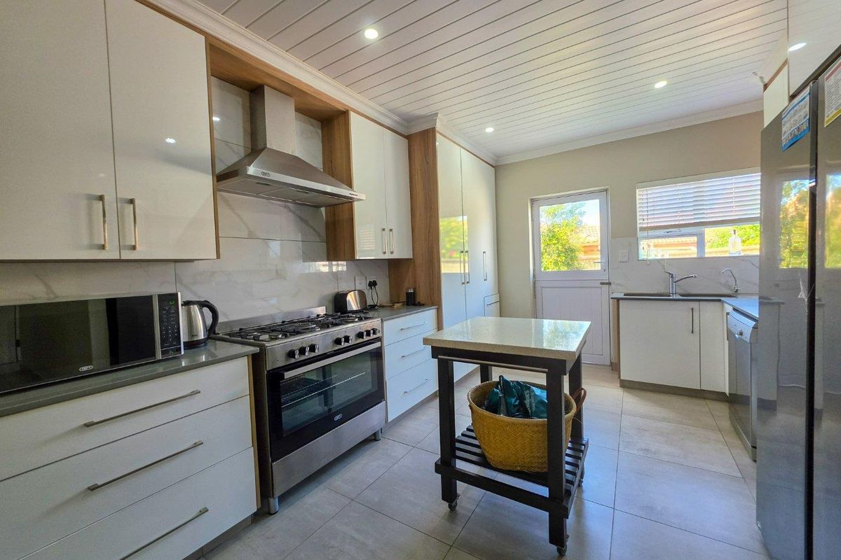 Modern kitchen featuring white cabinetry, stone countertops, gas stove with extractor fan, tiled flooring, and a bright, functional layout with direct outdoor access.