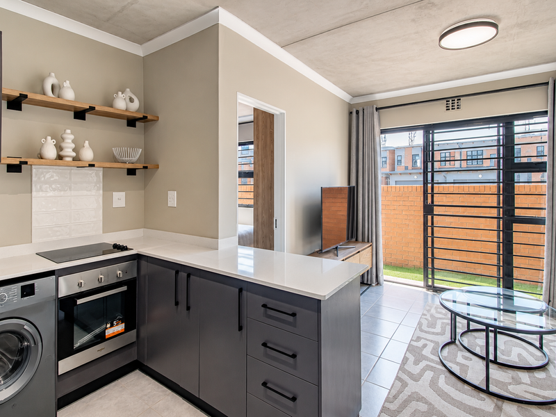 Modern open-plan kitchen and living area featuring sleek dark cabinetry, stone countertops, integrated appliances, and direct access to a private outdoor space.