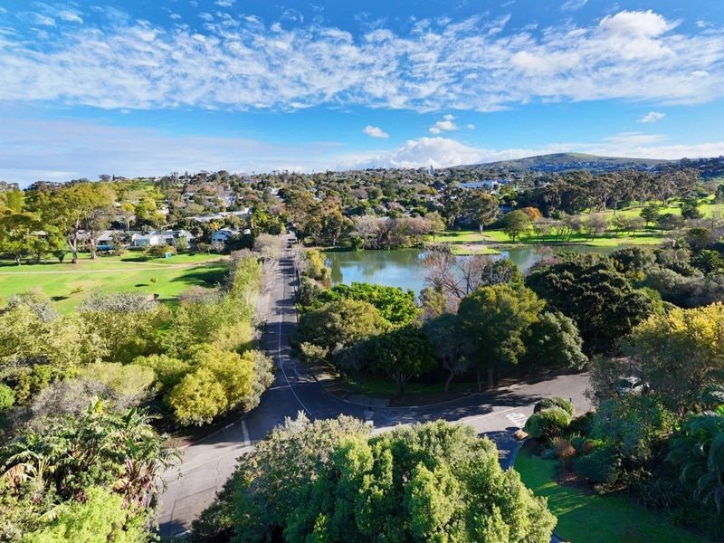 An elevated aerial view showcasing the surrounding neighbourhood, featuring lush green parklands, a scenic lake, and local road infrastructure.