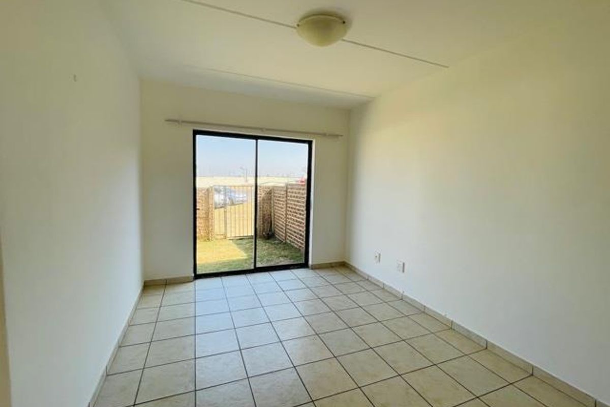 An empty living room featuring neutral tiled flooring and a sliding glass door providing direct access to a private outdoor area.