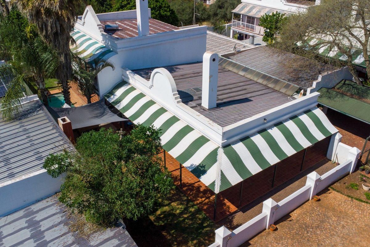 Aerial view of the property showcasing the roof structure, striped awnings, paved driveway, and surrounding garden area.