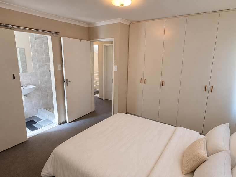 A well-maintained bedroom featuring extensive built-in cupboards, neutral carpeting, and direct access to an en-suite bathroom.