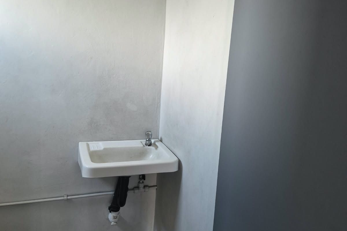 A minimalist bathroom space featuring a wall-mounted basin with exposed plumbing and simple, painted wall finishes.