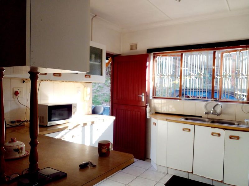 A functional kitchen featuring white cabinetry, laminate countertops, tiled flooring, and a window with security bars, offering a dated but practical layout.