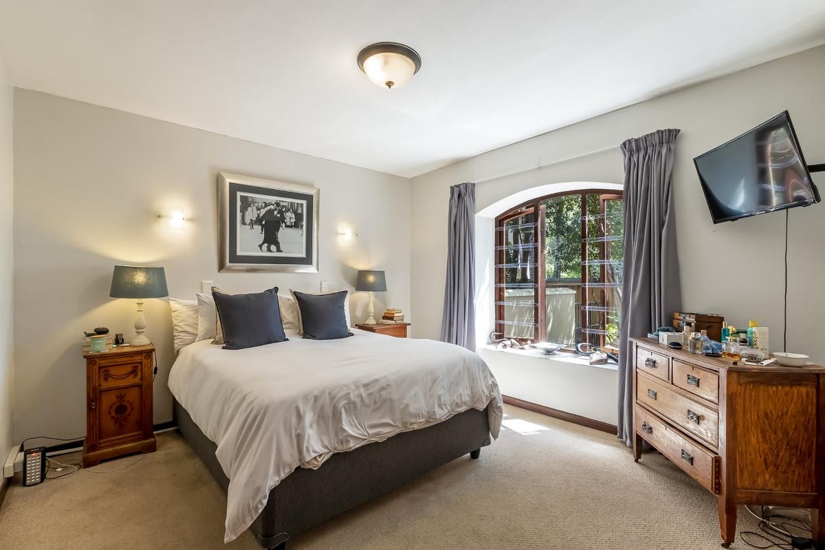 A well-lit bedroom featuring an arched window, neutral wall finishes, carpeted flooring, and integrated wall sconce lighting.