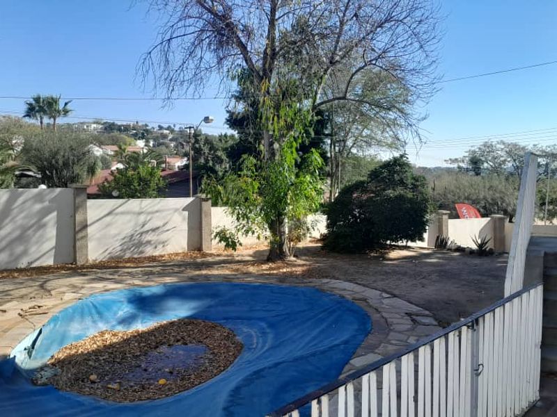 Outdoor pool area featuring a concrete staircase, metal safety railing, and perimeter walling, requiring landscaping and pool maintenance.