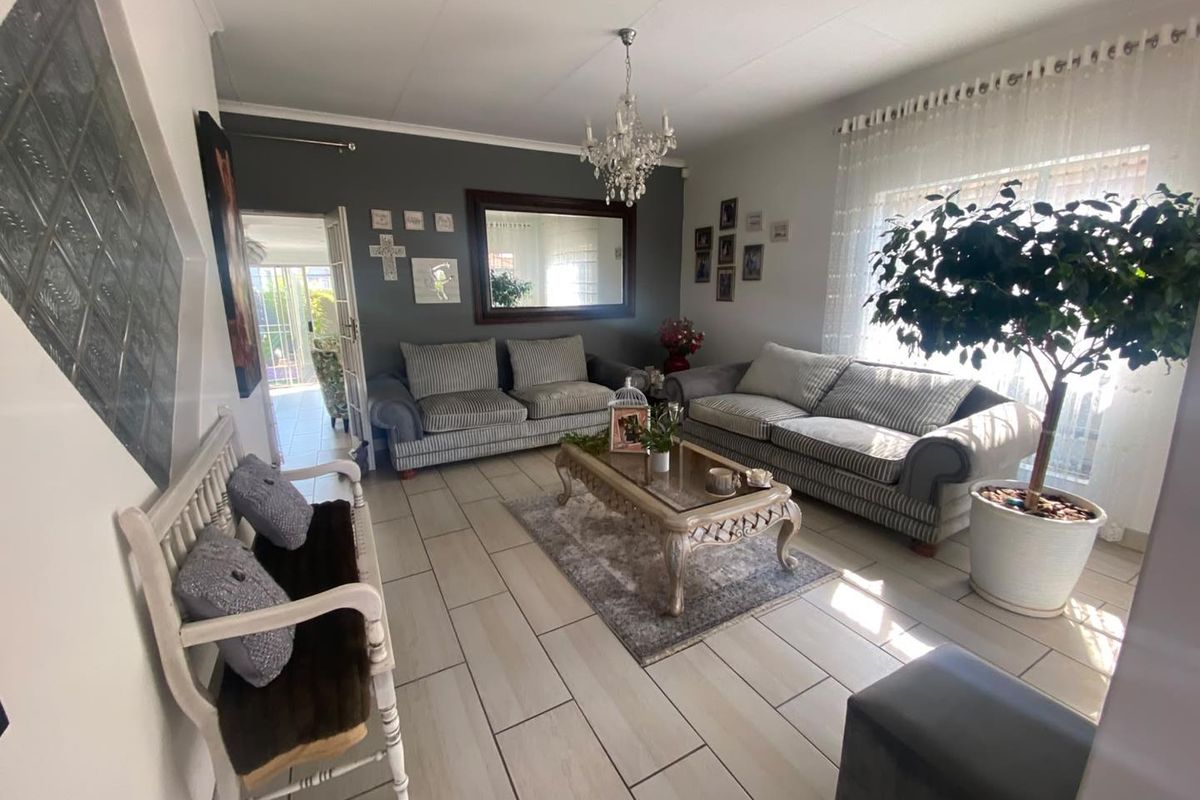 A well-maintained living room featuring light-toned tiled flooring, a decorative crystal chandelier, and a unique glass block feature wall.