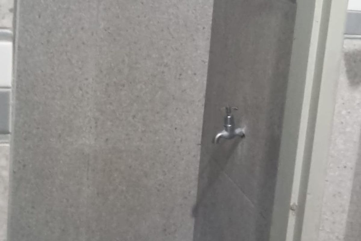 A compact shower area featuring grey wall tiles with a decorative mosaic border and a checkered floor tile pattern.