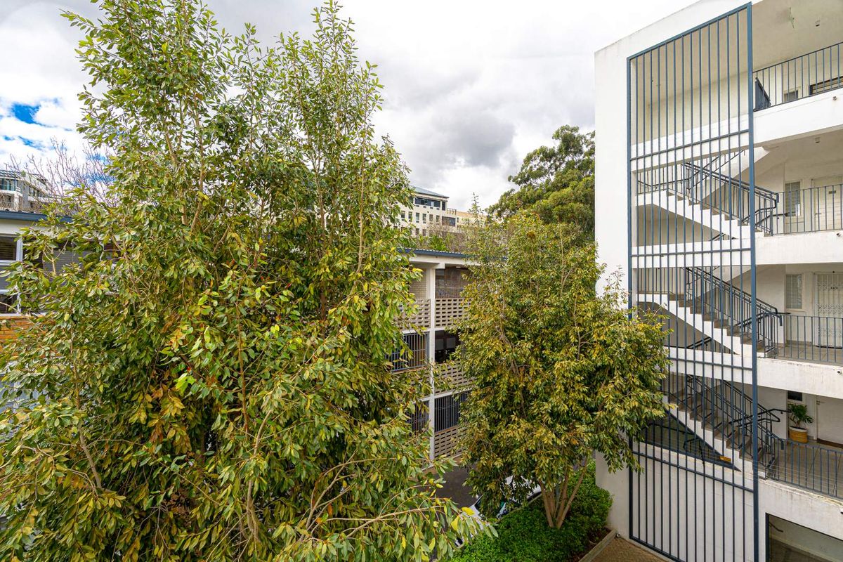 Exterior view of an apartment complex featuring a multi-level open-air stairwell, metal security screening, and established trees within the building courtyard.