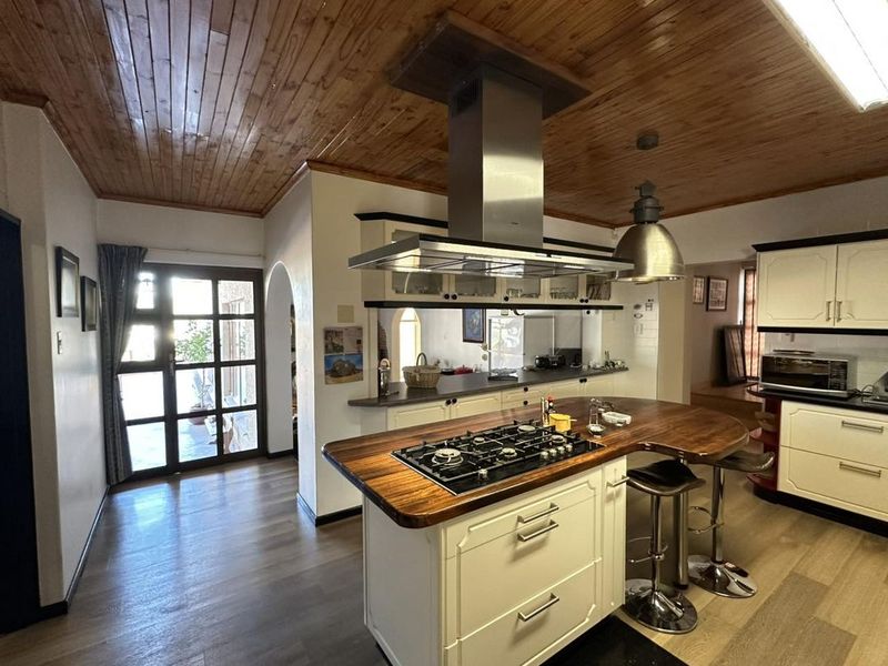 A spacious kitchen featuring a central island with a gas cooktop, stainless steel extractor fan, timber ceiling, and ample built-in cabinetry.