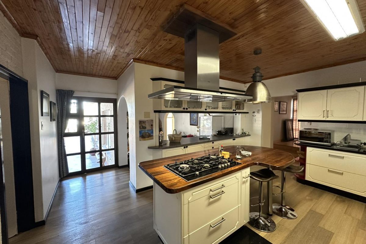 A spacious kitchen featuring a central island with a gas cooktop, stainless steel extractor fan, timber ceiling, and ample built-in cabinetry.