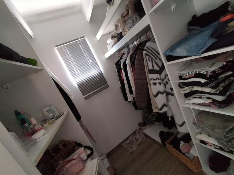 A functional walk-in closet featuring extensive built-in shelving and hanging rails, providing efficient storage space with natural light from a window.