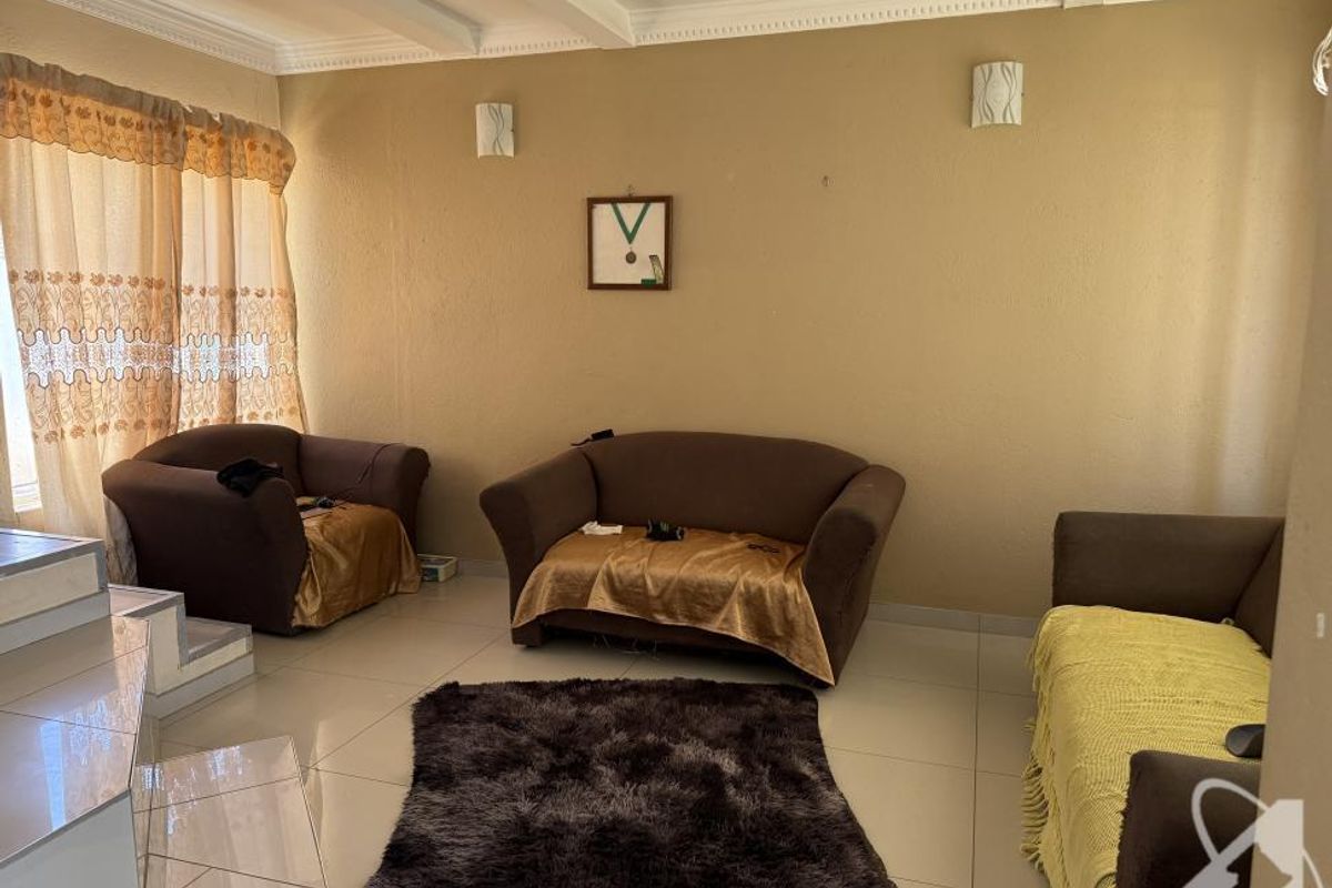 A spacious living room featuring tiled flooring, recessed ceiling details, and large windows allowing for natural light.