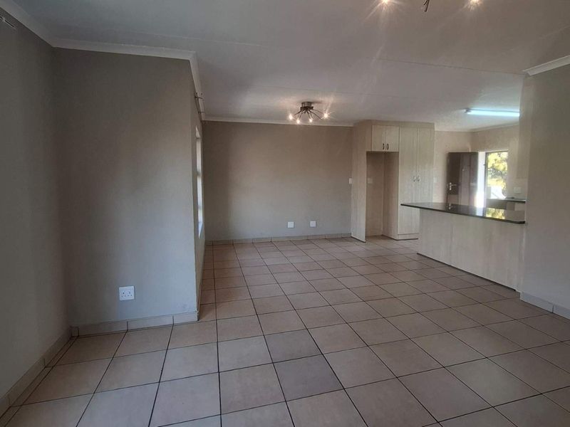 Spacious open-plan living and kitchen area featuring neutral tiled flooring, modern cabinetry, and a breakfast bar, offering a versatile layout for living and dining.